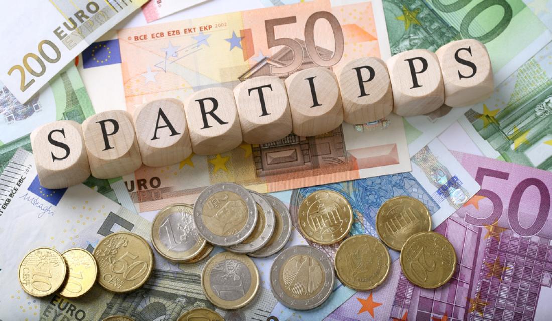 Würfel bilden das Wort Spartipps auf einem Haufen Geldscheinen und Münzen