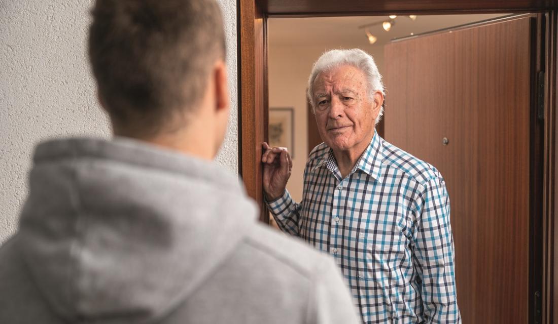 Älterer Mann öffnet seine Wohnungstür. Davor steht ein junger Mann.