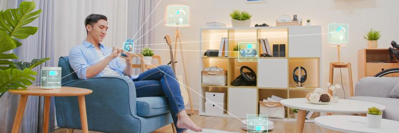 Person sitzt in ihrem Wohnzimmer mit Smartphone in der Hand und steuert verschiedene smarte Geräte an