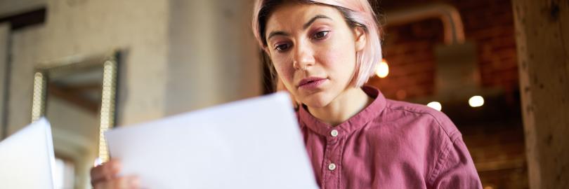 Eine junge Frau hält mit besorgtem Gesicht einen Brief in der Hand und liest 