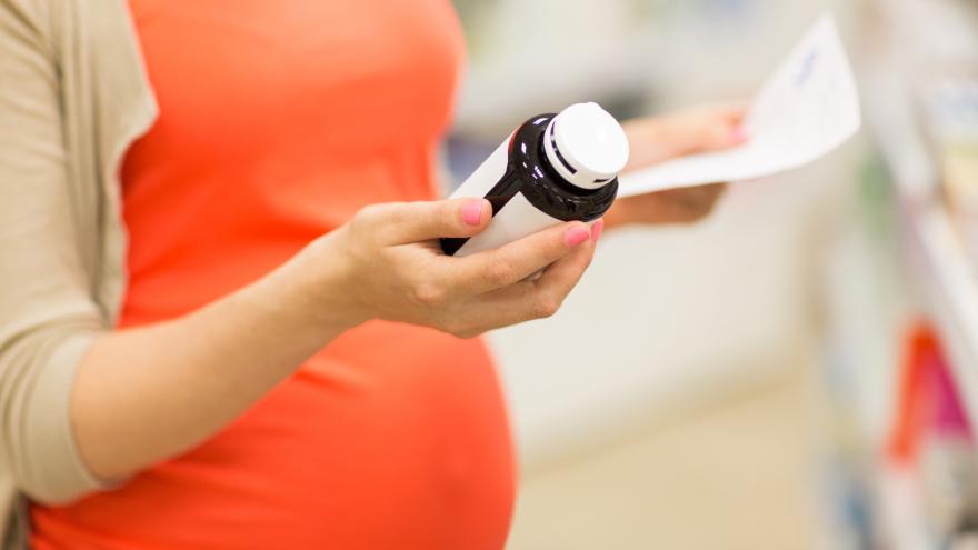 Schwangere hält Packung mit Nahrungsergänzungsmitteln in der Hand
