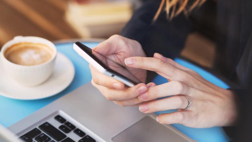 Eine Person sitzt am Laptop und Smartphone und der Hand am Tisch