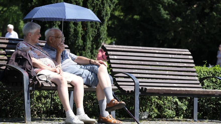 Ein älteres Pärchen sitzt auf einer Parkbank unter einem Regenschirm 