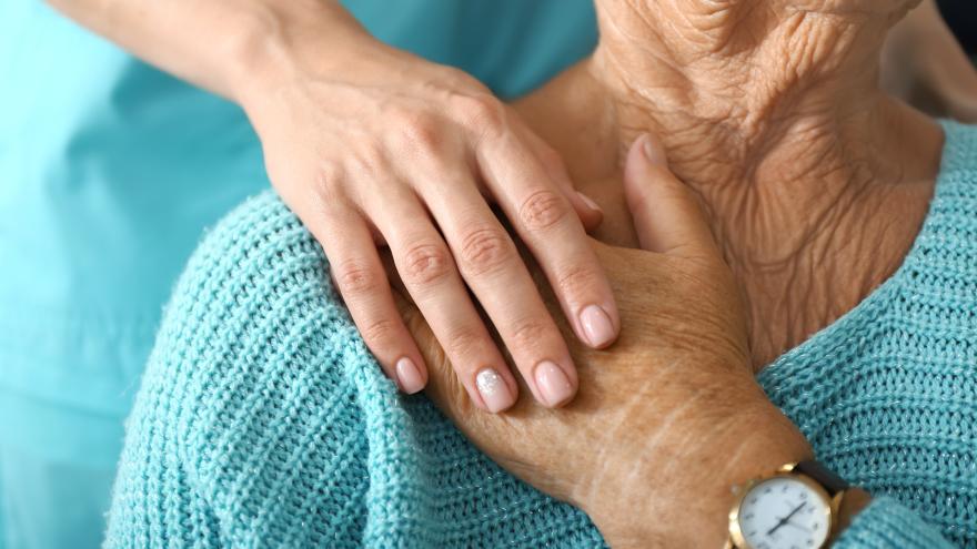 Frau legt ihre Hand auf ihre Schulter. Eine Person hinter ihr fasst ihre Hand