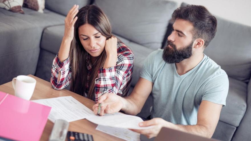 Ein Paar sitzt vor dem Wohnzimmertisch mit Finanzunterlagen und ist unzufrieden