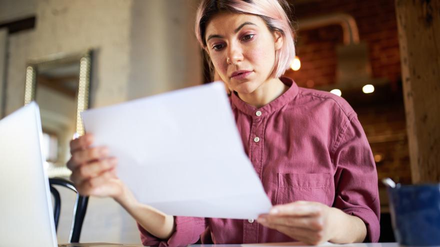Eine junge Frau hält mit besorgtem Gesicht einen Brief in der Hand und liest 
