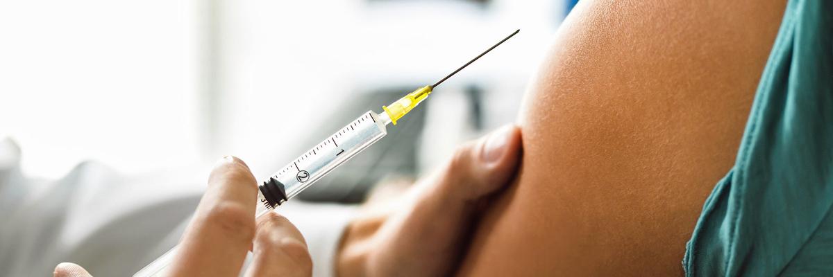 Impfspritze wird an einen Oberarm gehalten