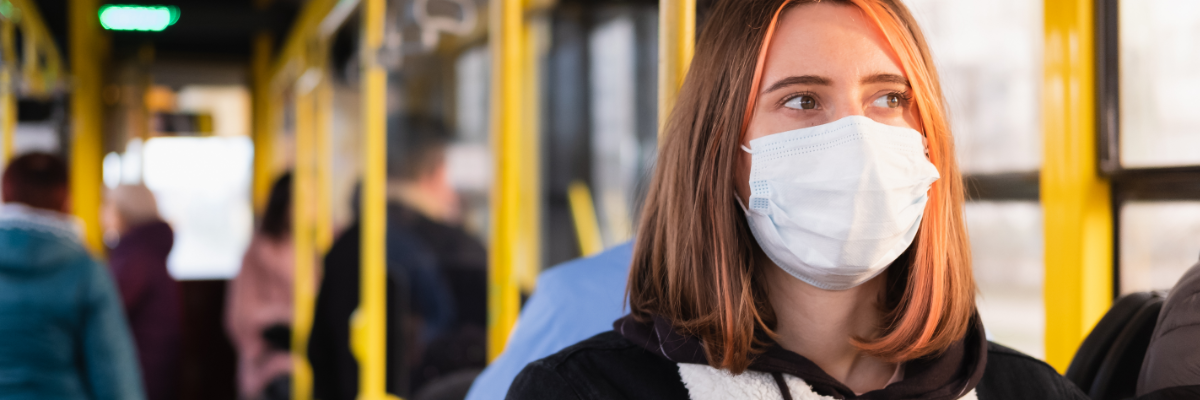Eine Frau sitzt in einem Bus und  trägt eine Schutzmaske.