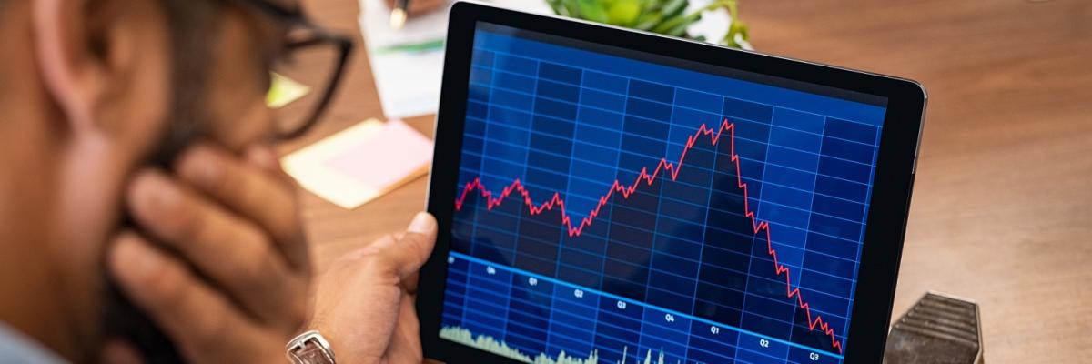 Mann schaut auf Tablet, das fallende Kurse anzeigt