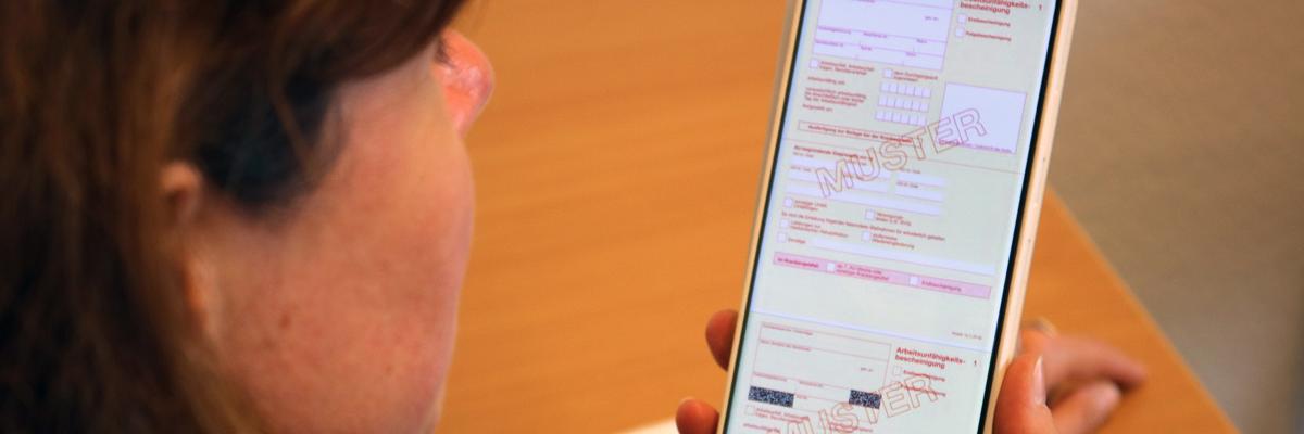 Frau hält Smartphone mit Arbeitsunfähigkeitsschein in der Hand