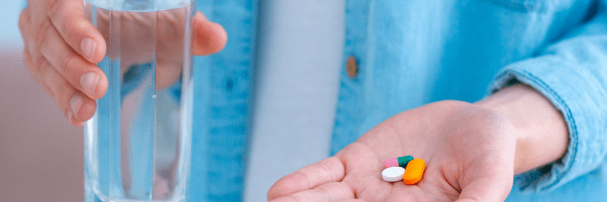 Jemand hält Tabletten in einer Hand und in der anderen ein Glas Wasser.