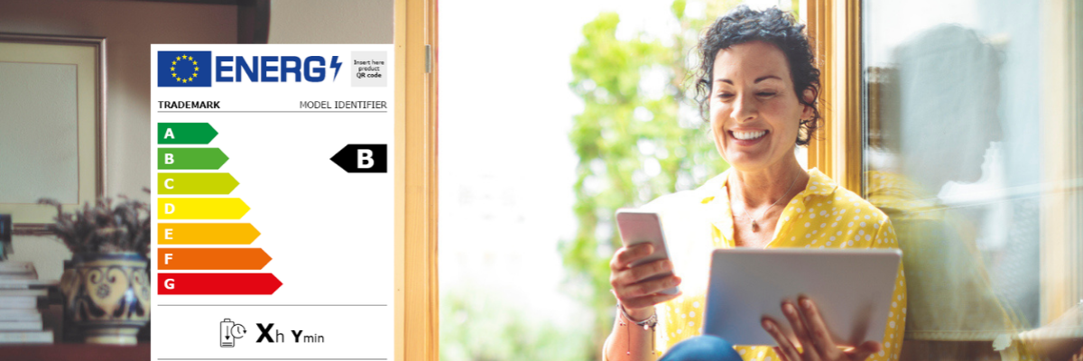 Frau am Fenster mit Tablet und Smartphone in der Hand, links im Bild das Energielabel für Smartphones und Tablets