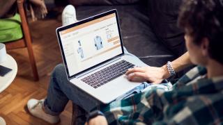 Eine Person mit Laptop auf dem Schoß, auf dem Bildschirm ist eine Online-Shop zu sehen.